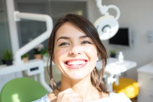 A confident person with a bright, white smile, showing healthy teeth in a modern dental clinic setting, soft natural lighting, focus on the smile, clean and professional atmosphere