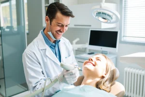 A modern dental clinic interior with a smiling dentist in a white coat using advanced painless dental technology, such as a laser device or computer-guided anesthesia system, treating a relaxed patient in a dental chair; soft, natural lighting, high detail, professional medical environment