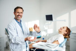 A calm, modern dental clinic interior with a smiling dentist in a white coat gently holding a dental implant model, a patient relaxed in the dental chair, soft natural lighting, clean white and light blue color scheme, subtle dental tools on a tray, no text or signs visible, focus on trust and comfort