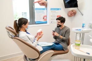 A clean, modern dental clinic interior with a dentist and a patient sitting in a dental chair, the dentist gently explaining oral hygiene using a model of teeth and gums, soft natural light from a window, educational posters about periodontitis prevention on the wall, toothbrush, floss, and mouthwash on a nearby tray, warm and reassuring atmosphere