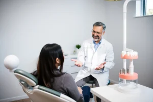 A calm, professional dental clinic interior with a dentist in a white coat explaining dental implant procedure to a patient sitting in a dental chair, showing a 3D model of a jaw with implants on a nearby table, soft natural lighting, clean and modern environment, focus on trust and clarity