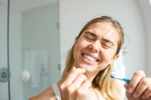 A person gently brushing their teeth with a soft-bristled toothbrush, smiling calmly, in a clean modern bathroom with natural light, no visible pain or discomfort, focus on proper brushing technique and relaxed expression